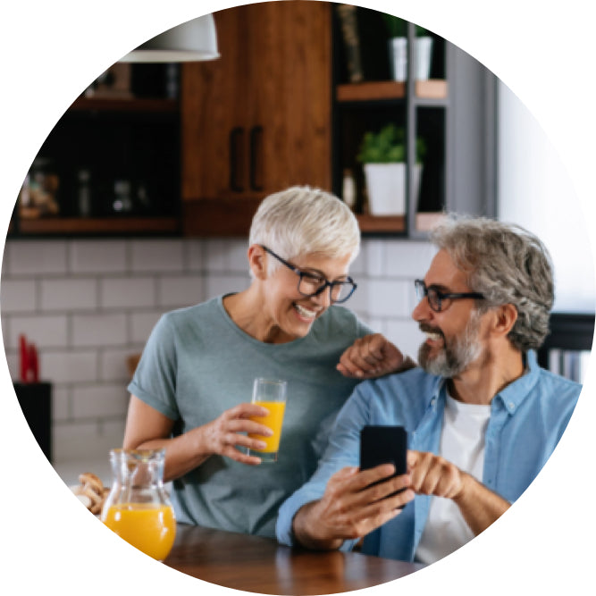 couple looking at smartphone and smiling, woman has a glass of juice